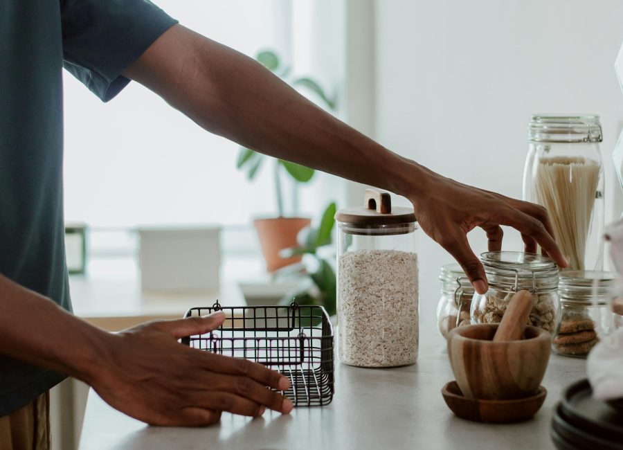 Close-up of hands arranging glass jars and utensils on a kitchen countertop.